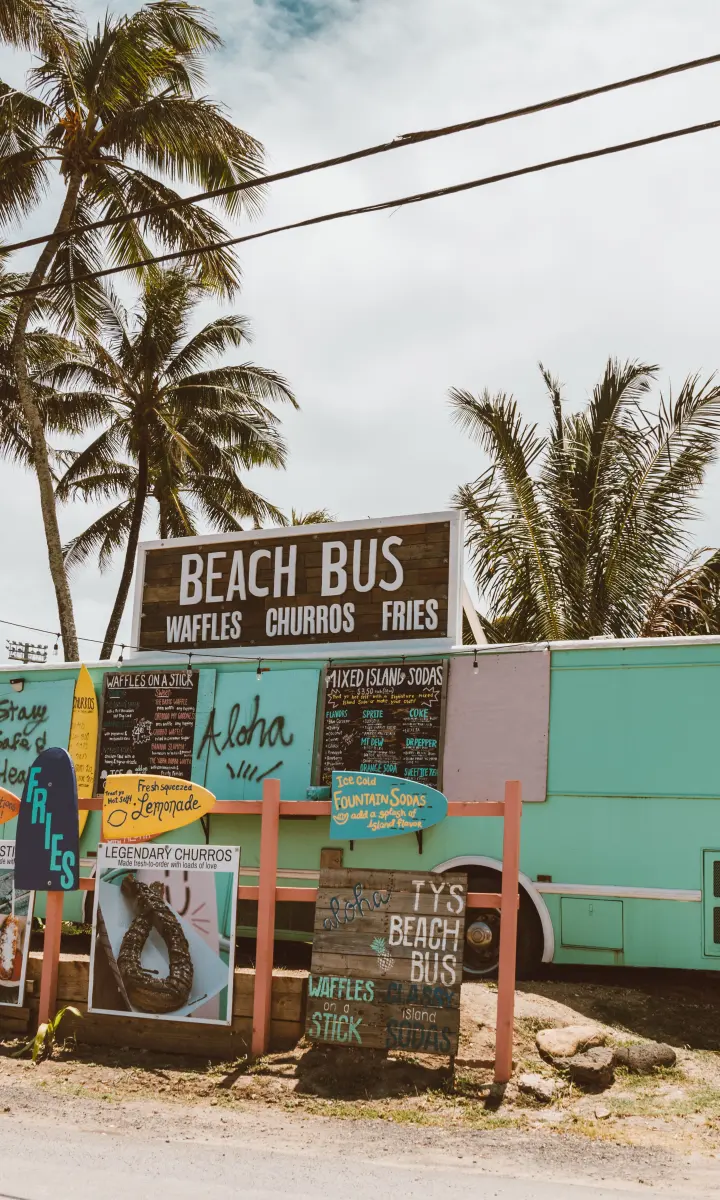 Colorful Beach Bus food truck beneath palm trees on Oahu's North Shore